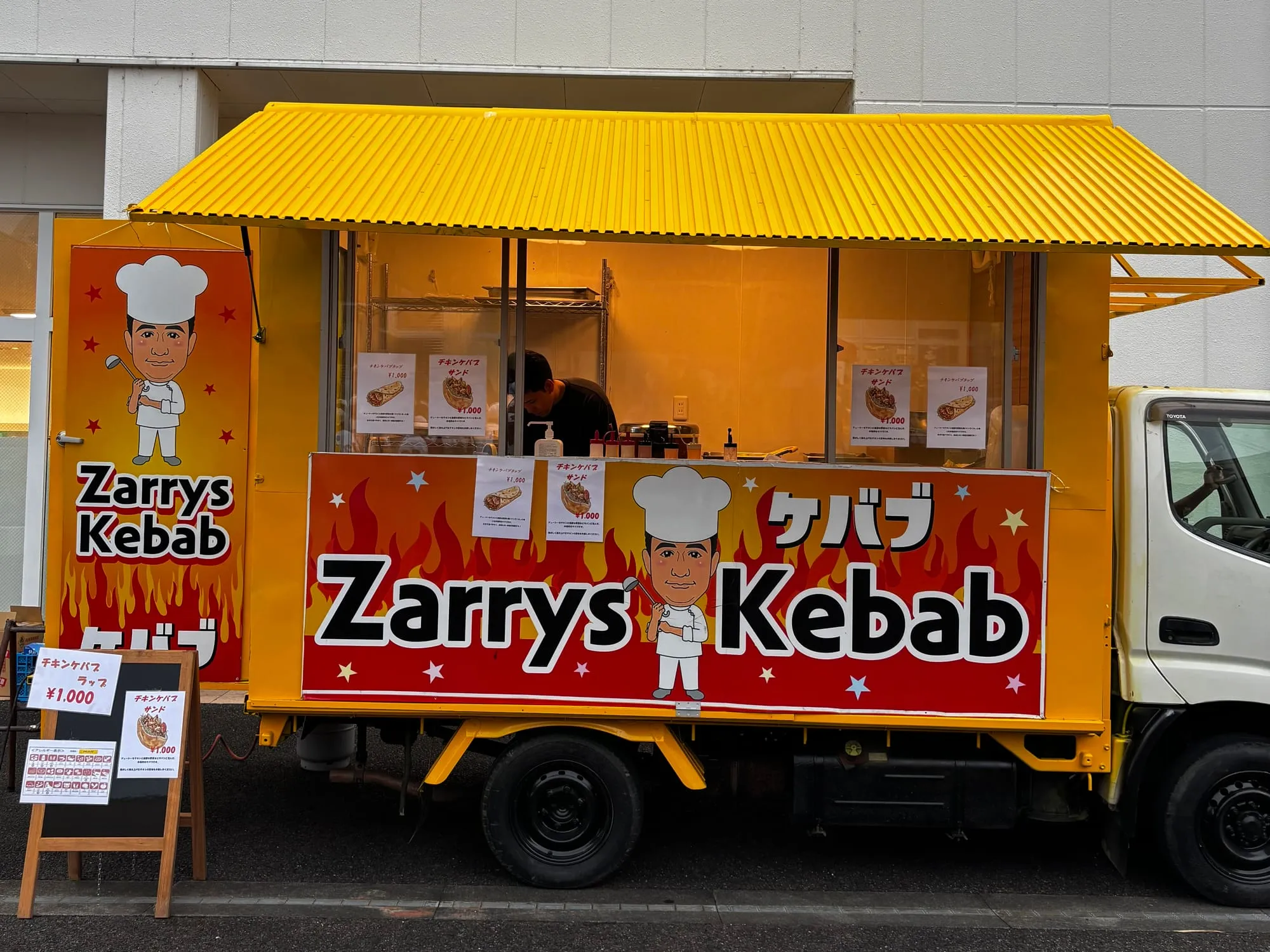 Zarrys Kebabの黄色いキッチンカー。赤い看板を掲げて営業している様子